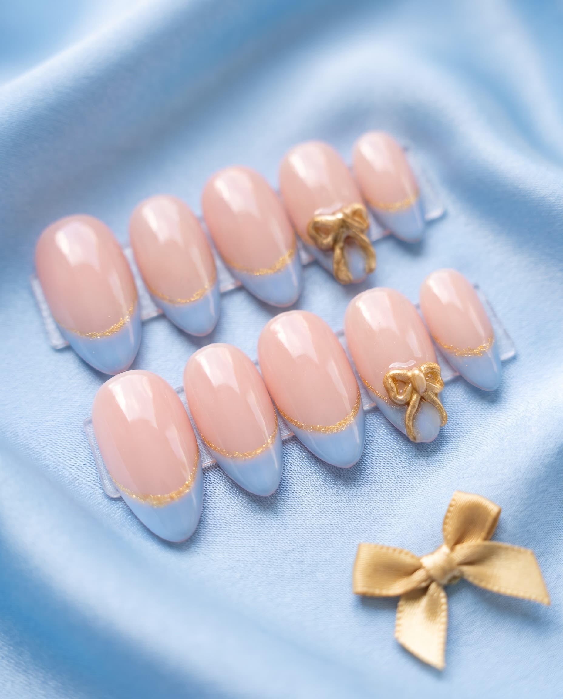 Baby Blue Bow — Nude base with a pastel-blue French tip, gold glitter line, and a gold 3D bow charm