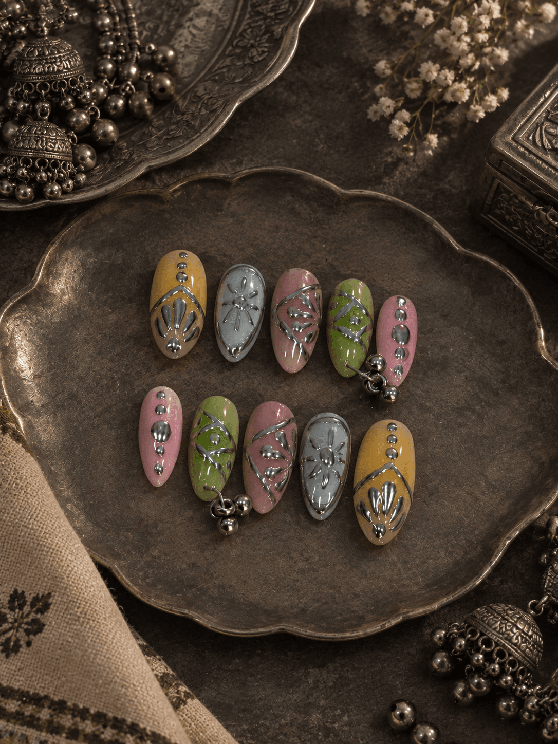 Silver Sringar — Pastel almond nails with silver chrome ethnic motifs and dangling bead charms.