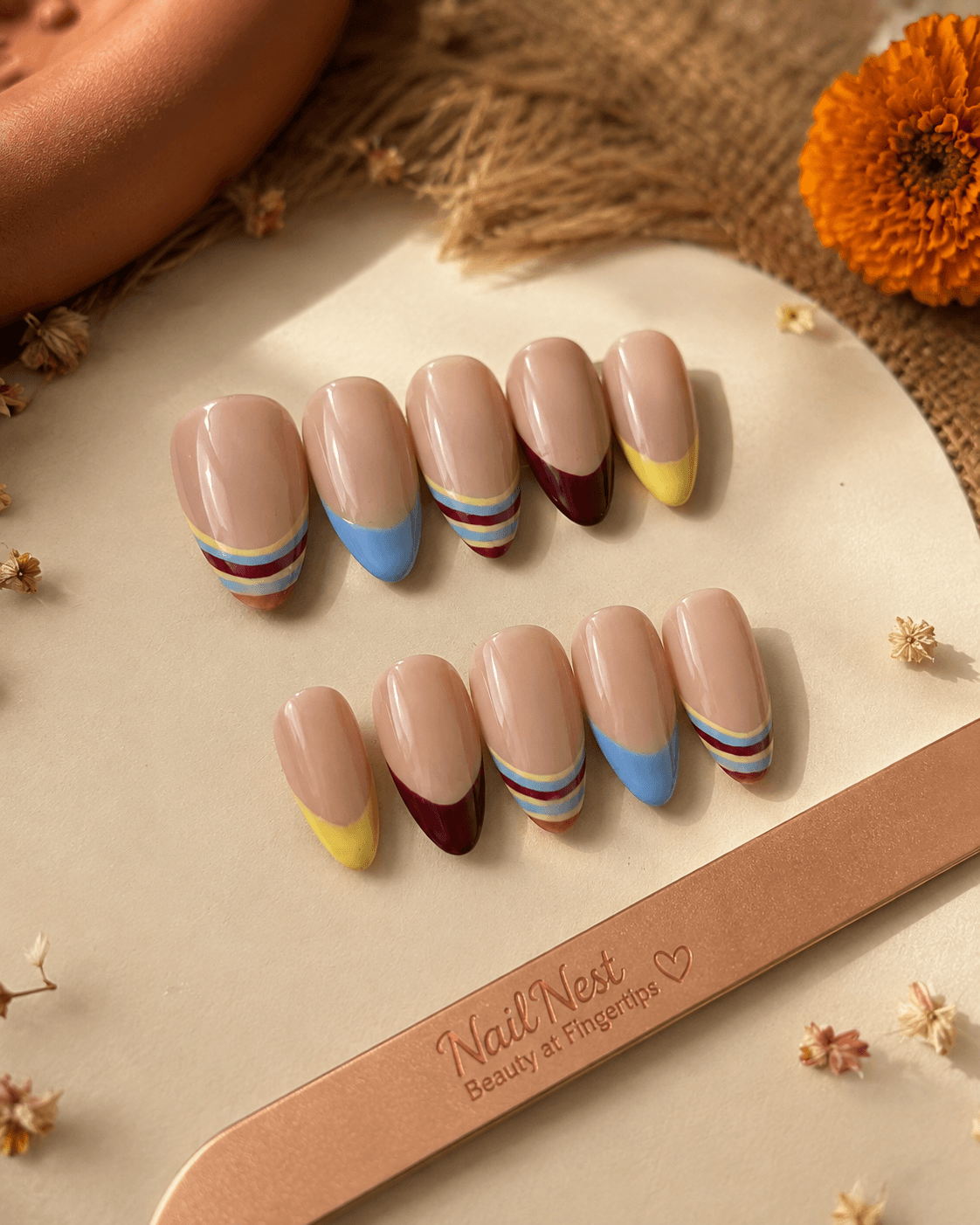 Whimsical Tips — Nude nails finished with playful striped color-block tips in burgundy, blue, and yellow